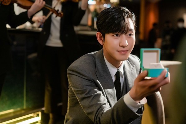 O ator Ahn Hyo-seop sorrindo de forma gentil usando terno corporativo cinza como Kang Tae-moo