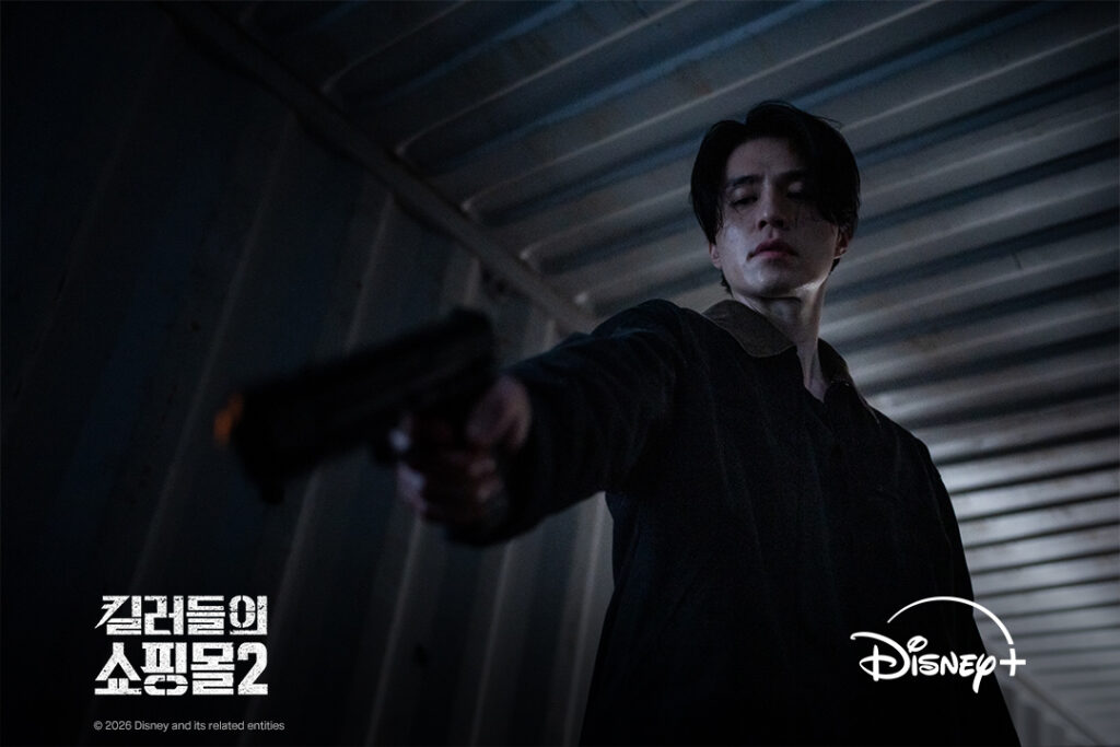 Lee Dong-wook como Jeong Jin-man aponta uma arma em ambiente industrial escuro em Uma Loja Para Assassinos 2