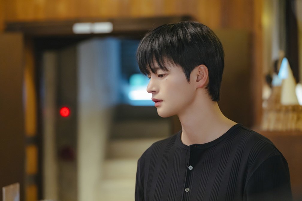 Seo In-guk como Kang Si-woo de suéter preto e cabelo natural em ambiente de bar em Te vejo no trabalho