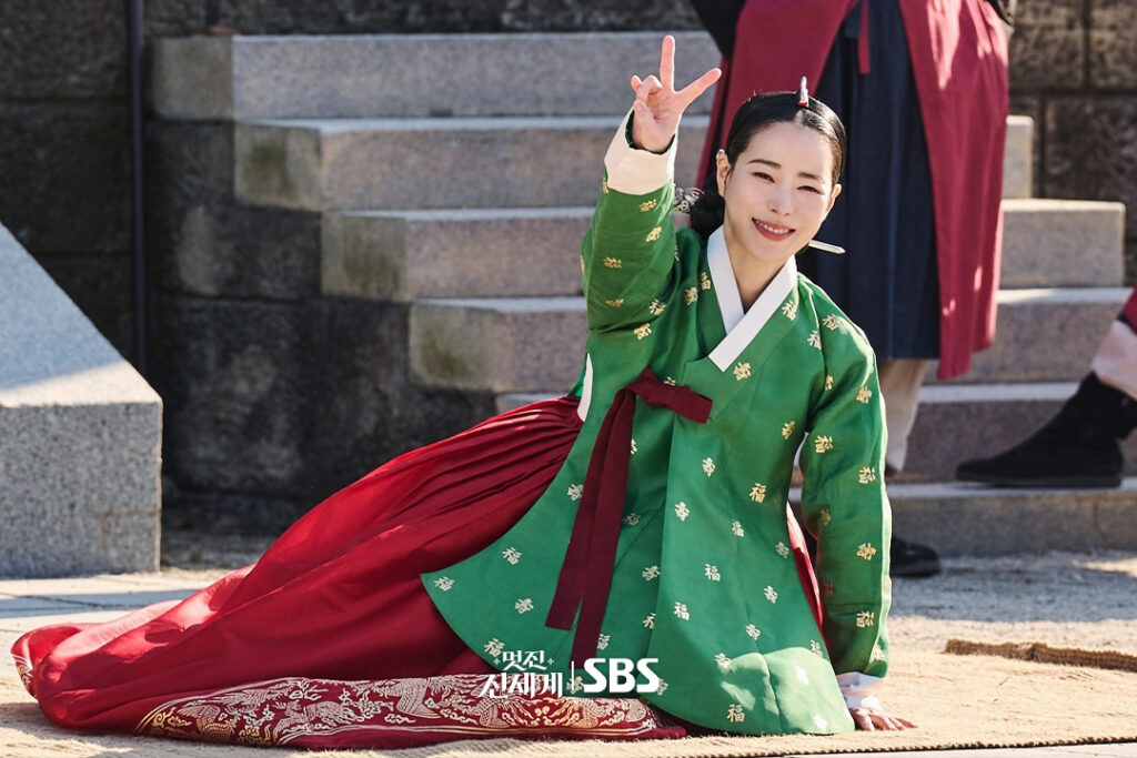 Lim Ji-yeon sorri e faz sinal de V nos bastidores das filmagens de My Royal Nemesis vestindo hanbok verde