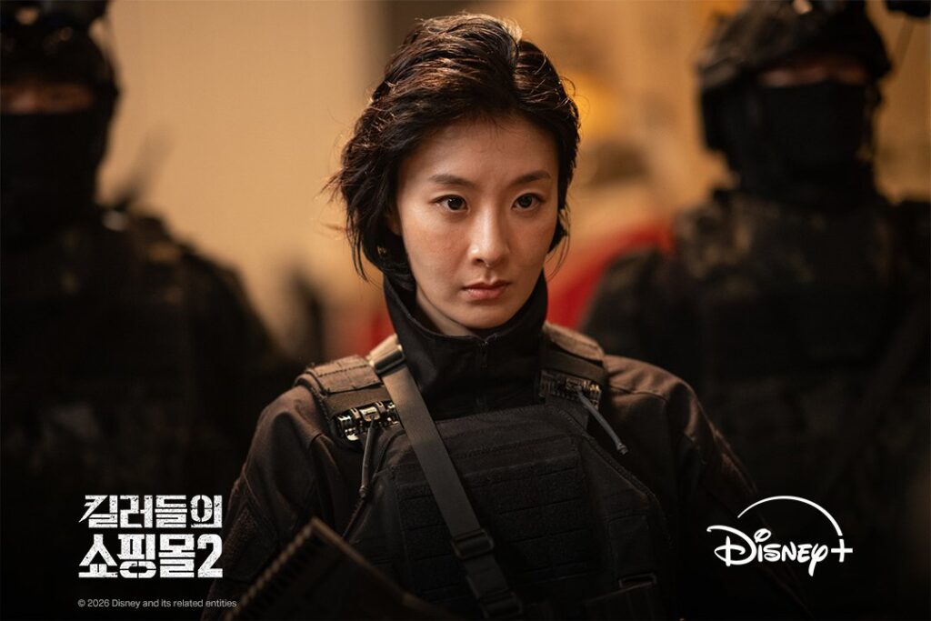  Hyunri como Q em equipamento tático ladeada por soldados mascarados em Uma Loja Para Assassinos 2
