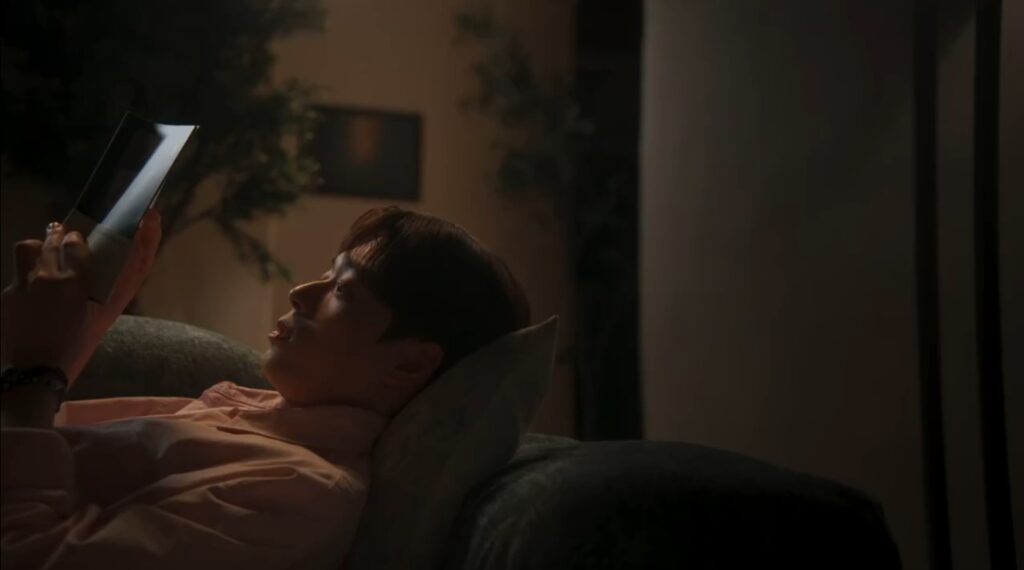 Chu Tae Jeong deitado no sofá lendo um tablet à noite