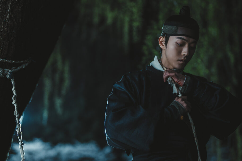 Nam Joo-hyuk como Gu-cheon caminha em direção a um lago com uma corda no pescoço em cena tensa de A Leste do Palácio