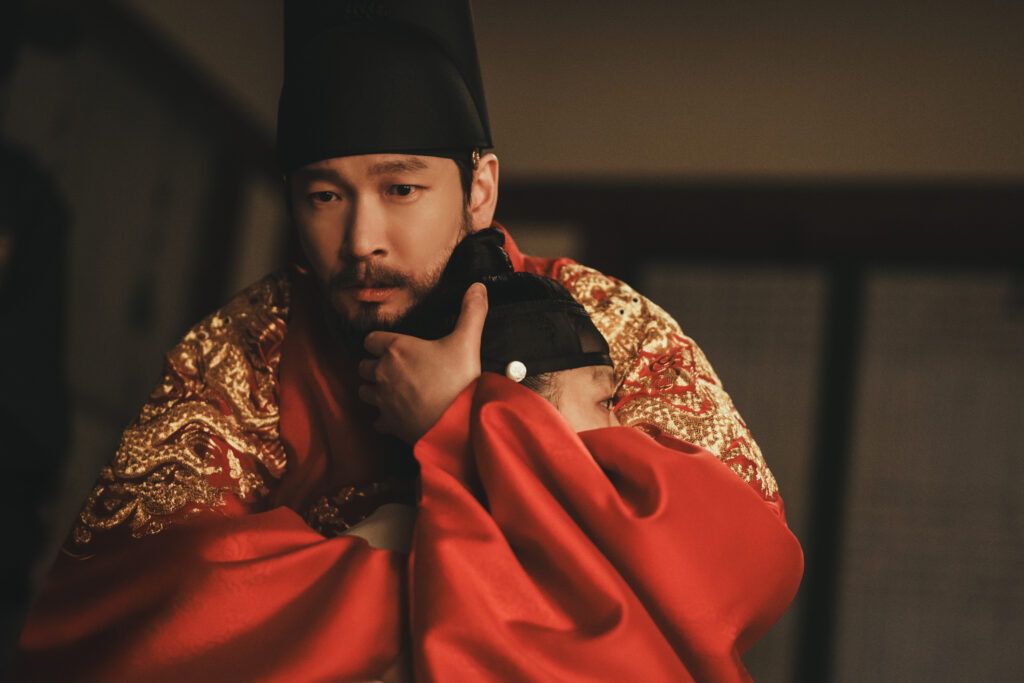 Cho Seung-woo como o Rei segura o Príncipe Yeongan nos braços com expressão de desespero em A Leste do Palácio