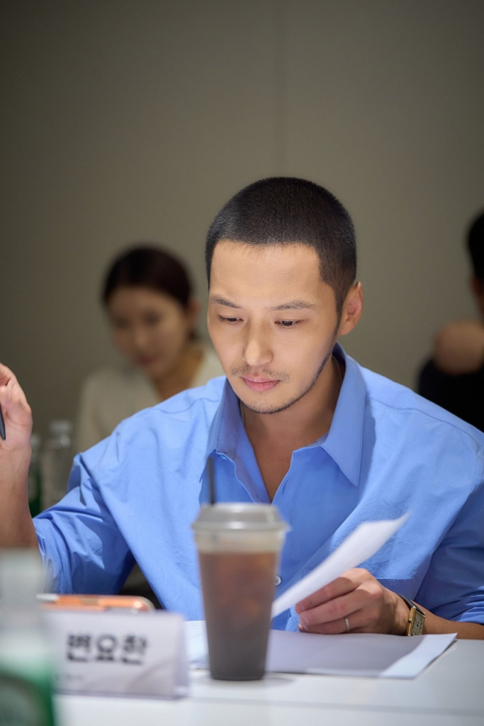 Byun Yo-han concentrado lendo o roteiro de Dia Sem Maus Espíritos durante sessão de leitura