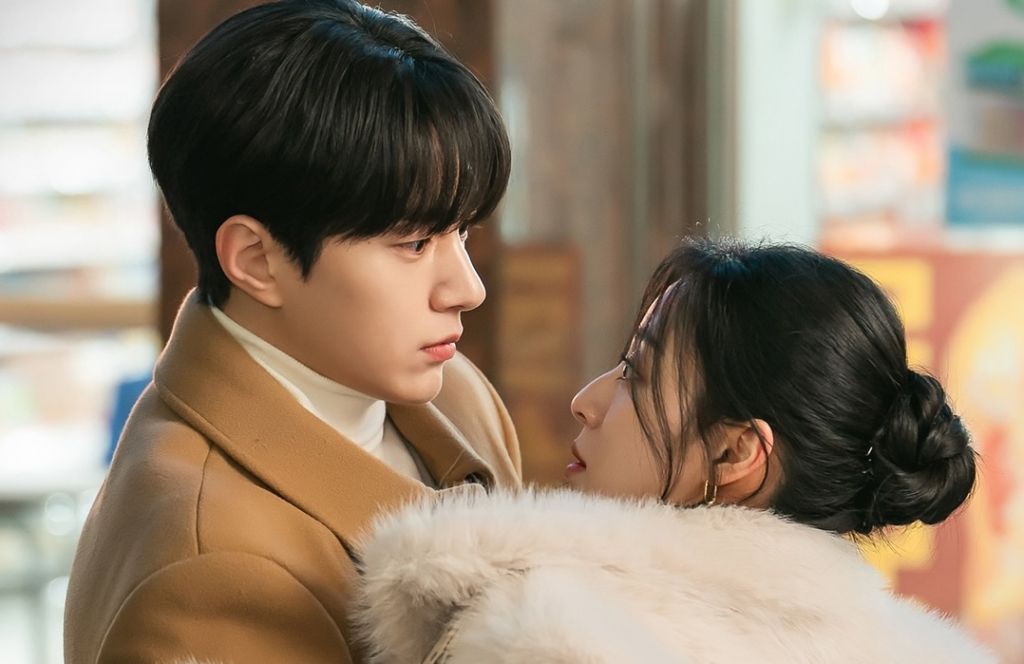 Kim Myung-soo olha de perto para Kang Min-ah, que está envolta em um casaco de pele, em still de Amor em Sincronia