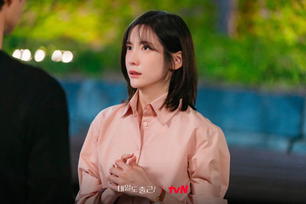 Park Ji-hyun como Cha Ji-yoon com expressão hesitante e mãos entrelaçadas em cena noturna de Te vejo no trabalho
